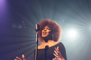 Photo shows a woman singing at a microphone Photo by Josh Rocklage